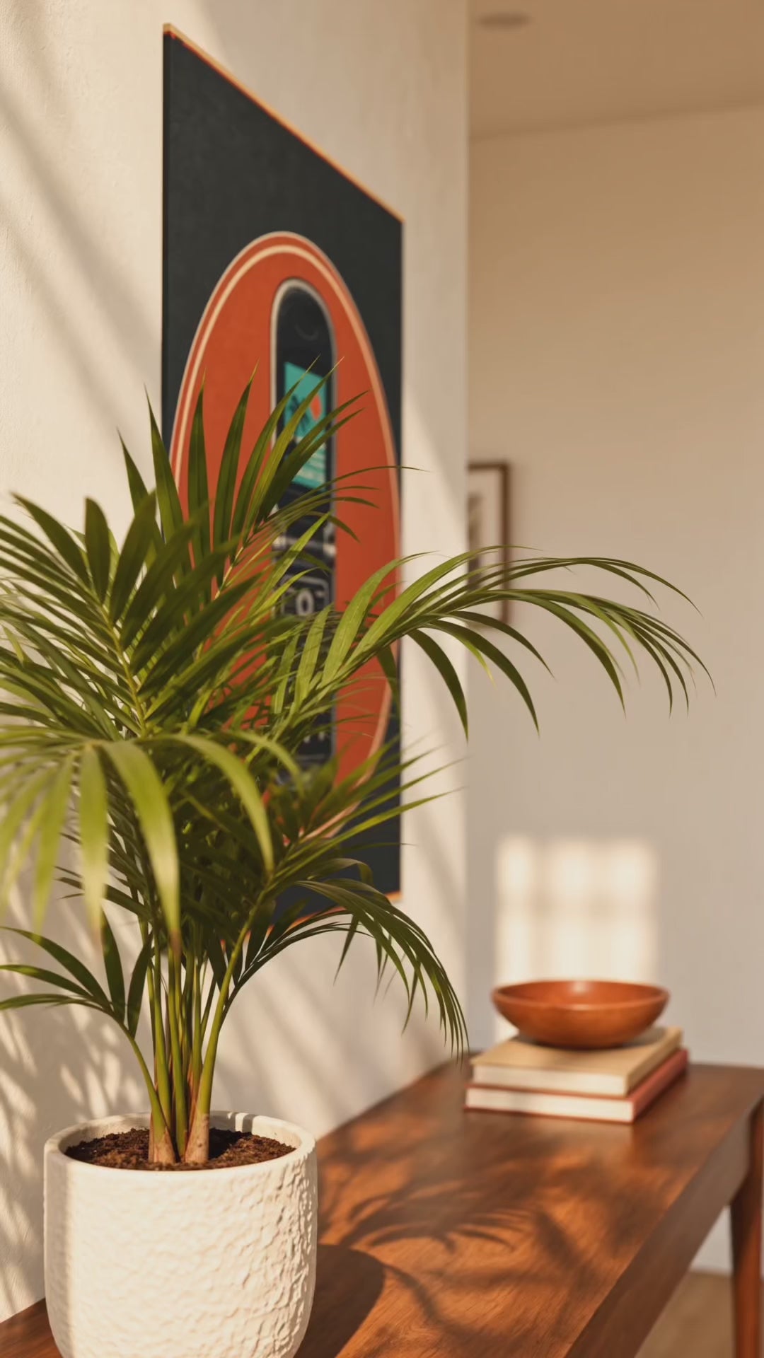 A framed wall art print featuring a retro flip phone inside an orange circle on a dark background, displayed above a wooden console table in a styled interior with a plant and ocean view.